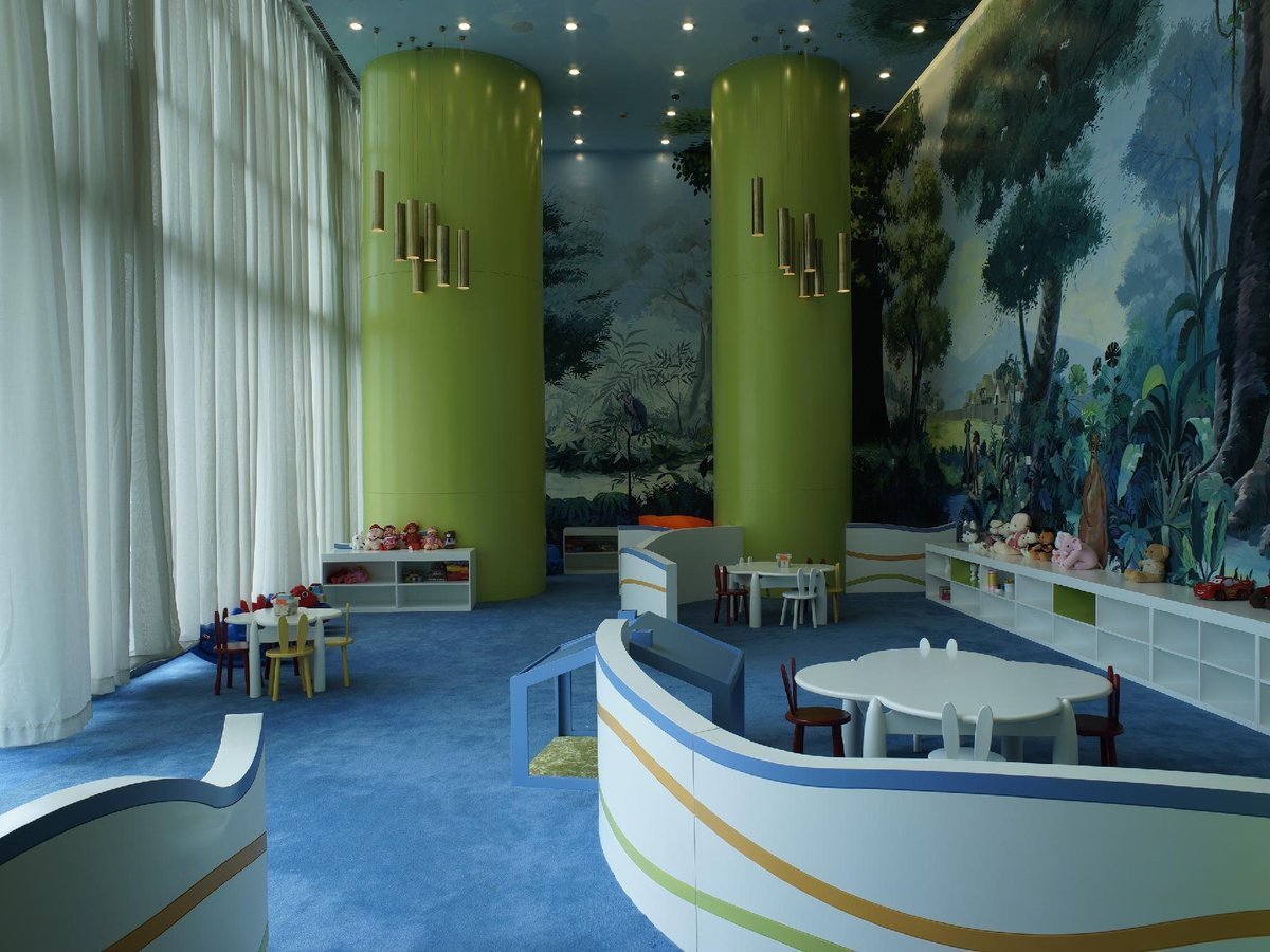 Bright indoor kids club with jungle murals, yellow pillars, a blue carpet and low craft tables