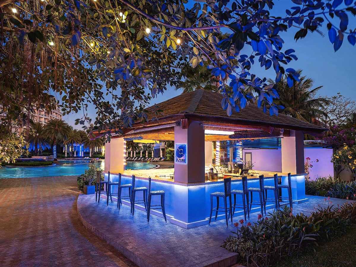 Thatched pool bar lit blue at night, with high stools beside the pool