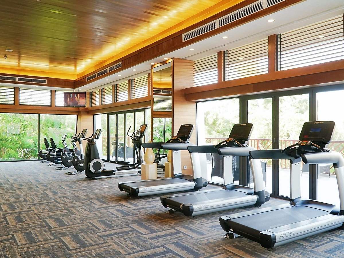 Gym with treadmills and weight machines facing glass walls and greenery outside