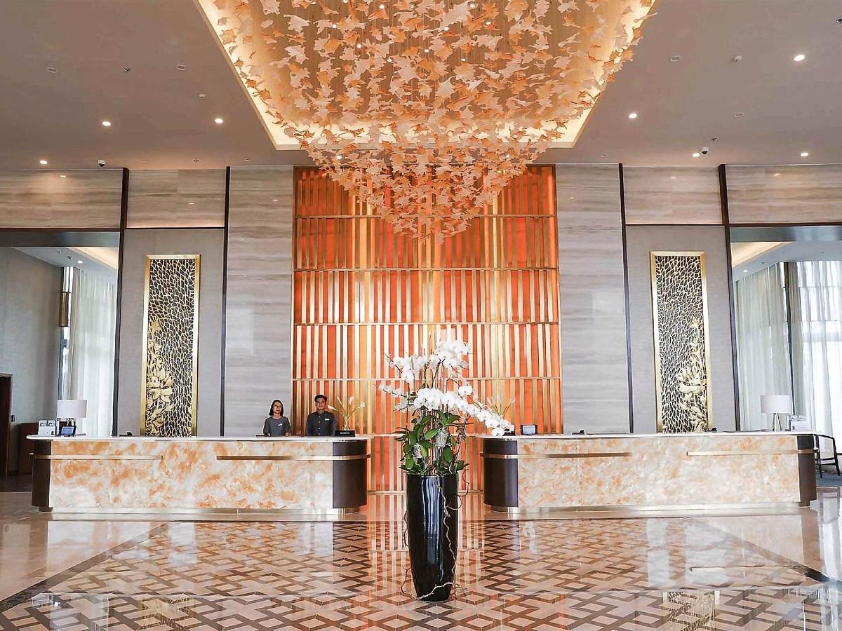 Reception desk of marble and amber glass, with a large orchid arrangement and a golden chandelier above