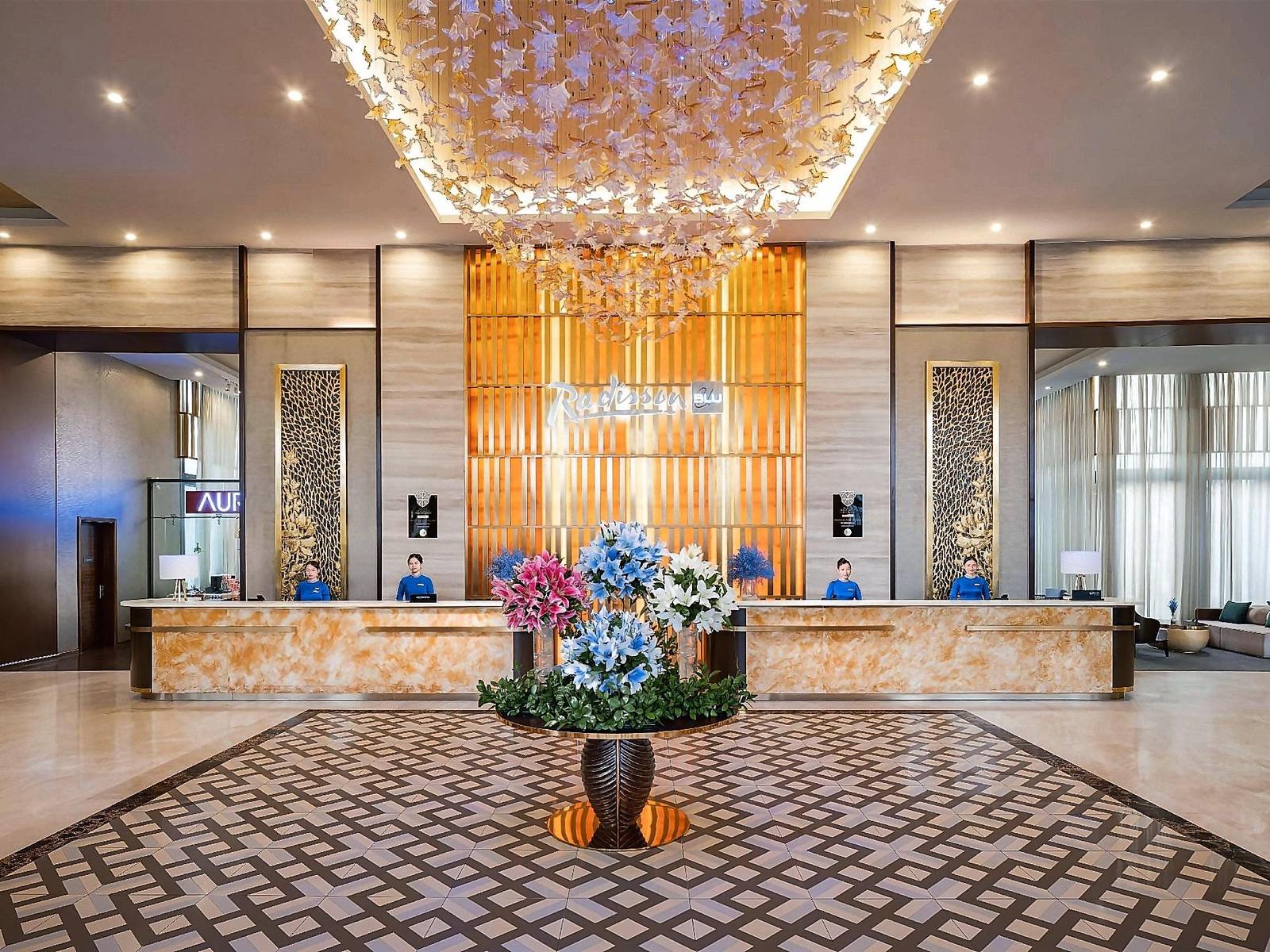 Lobby with a patterned marble floor, a golden chandelier and an amber-lit reception desk