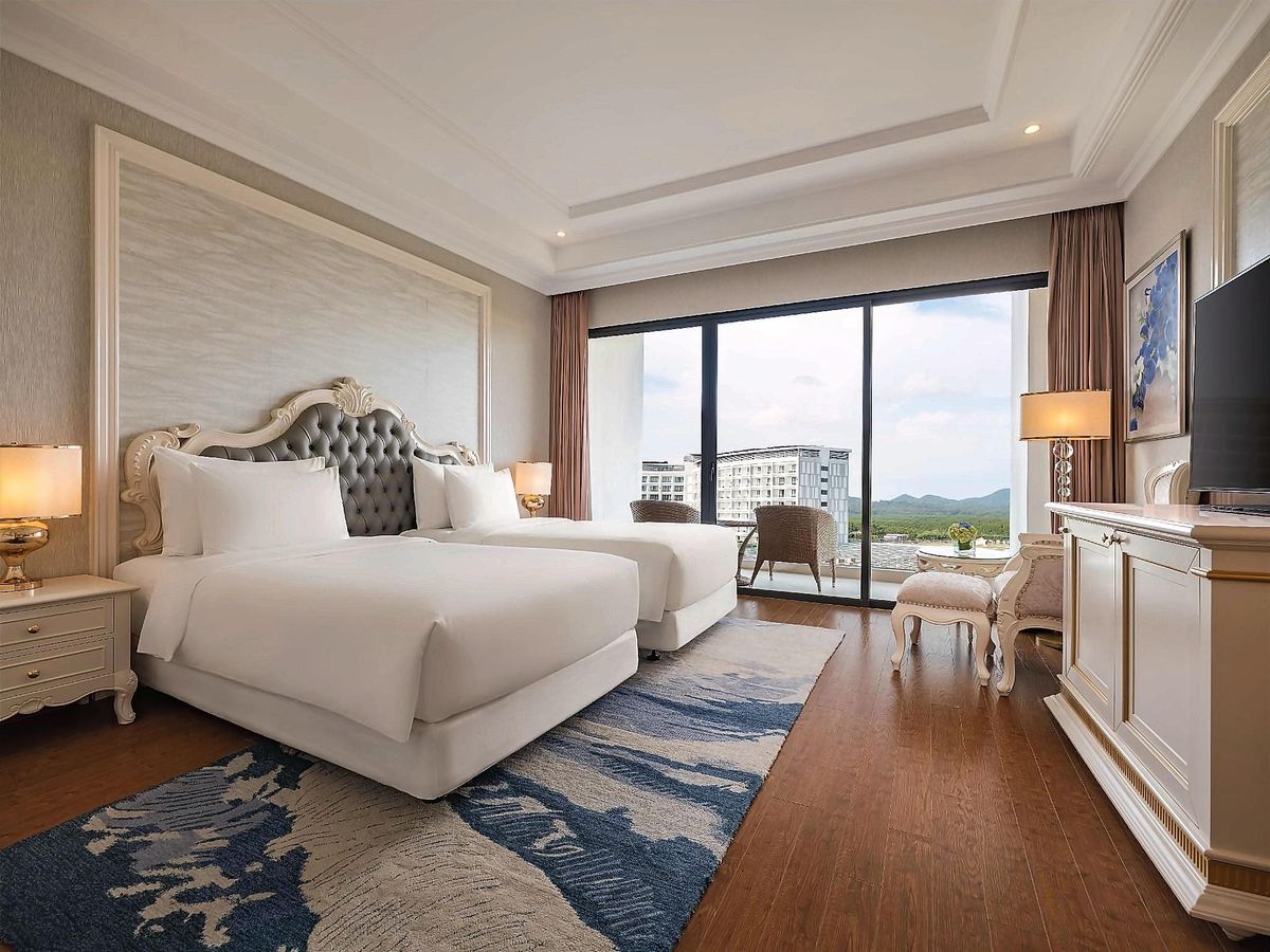 Deluxe room with two beds and a balcony looking out at neighbouring hotel buildings and hills