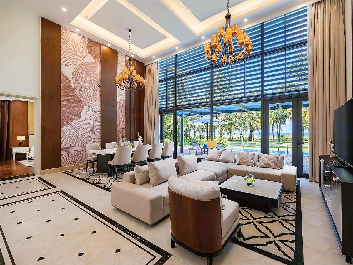 Double-height villa living room with a chandelier, white sofas and tall windows onto the garden