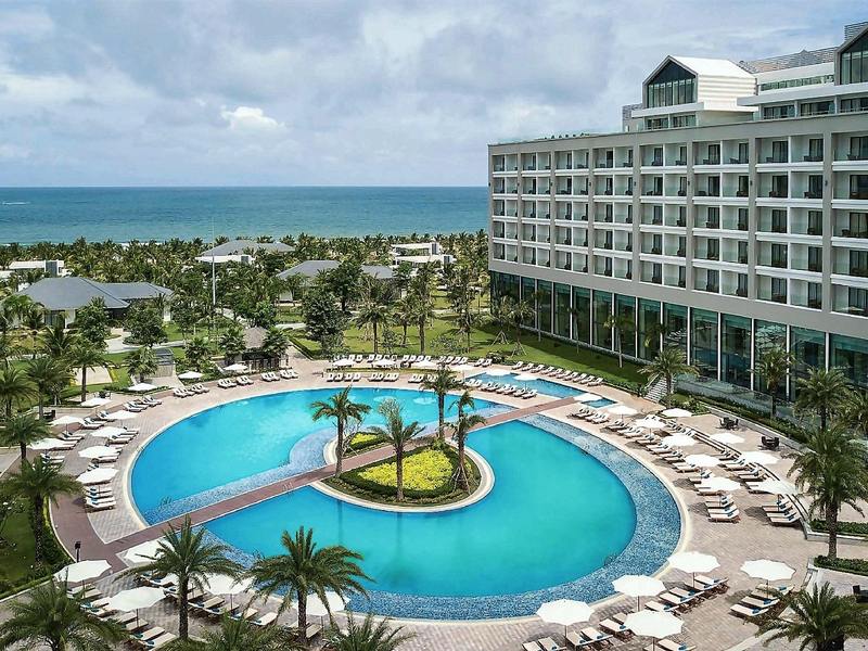Curving lagoon pool around a palm-planted island, with white parasols and the resort building alongside