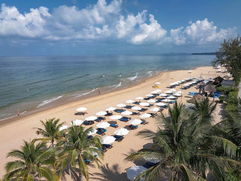 Rows of white parasols and loungers along a long sandy beach, with palm trees in the foreground