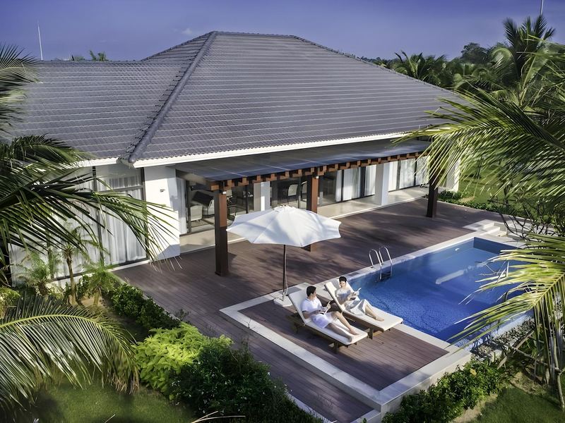 Aerial view of a villa with a grey hipped roof and a private rectangular pool among palm trees